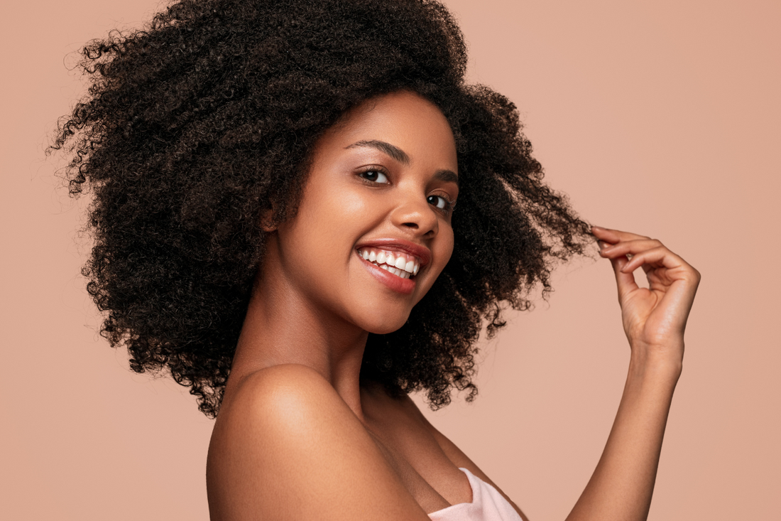 Smiling woman with voluminous natural Type 4 hair and glowing skin, eyes closed and head tilted slightly, radiating joy and confidence in her texture.
