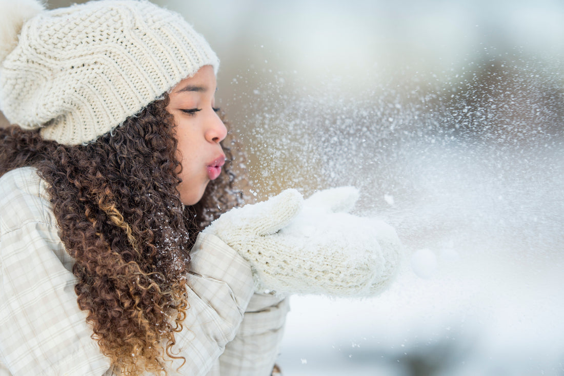 teenage-girl-with-curly-hair-standing-outside-during-winter-blowing-snow-off-her-gloves