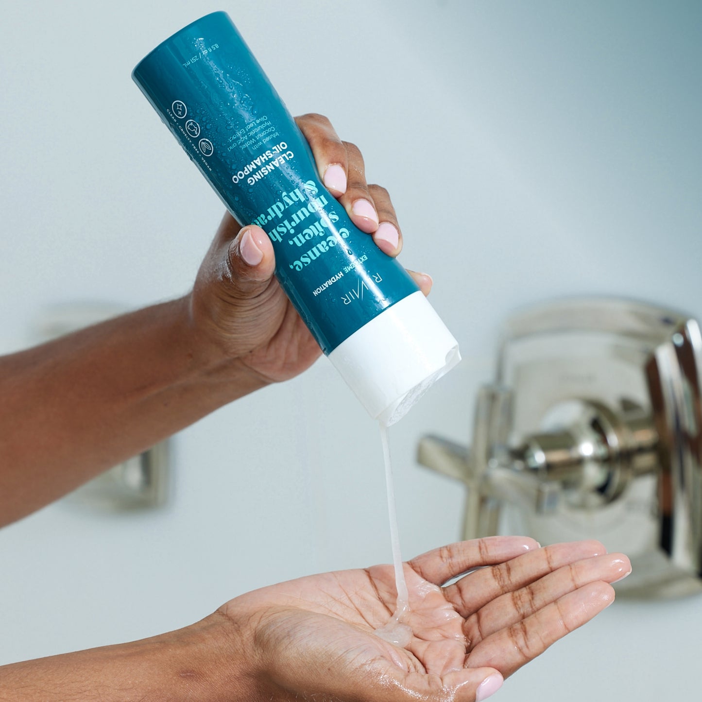 Woman in shower squeezing cleansing oil shampoo from bottle onto hand