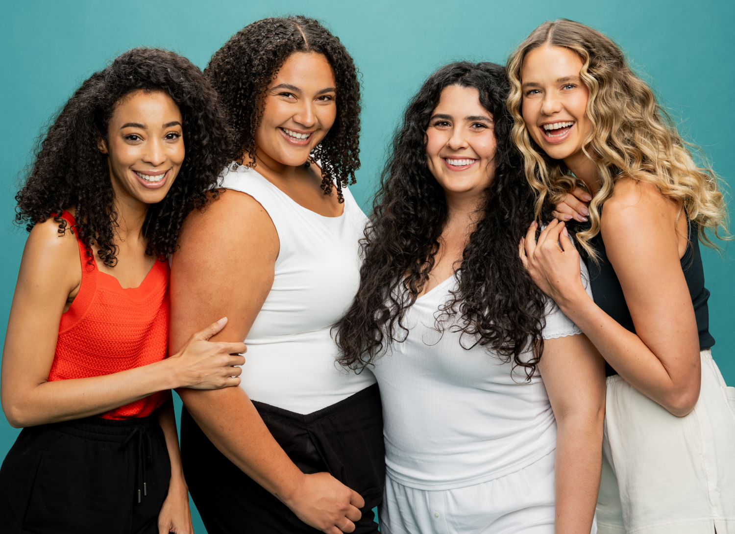 Diverse group of four women with hair ranging from tight curls to loose curls pose together before using the RevAir dryer