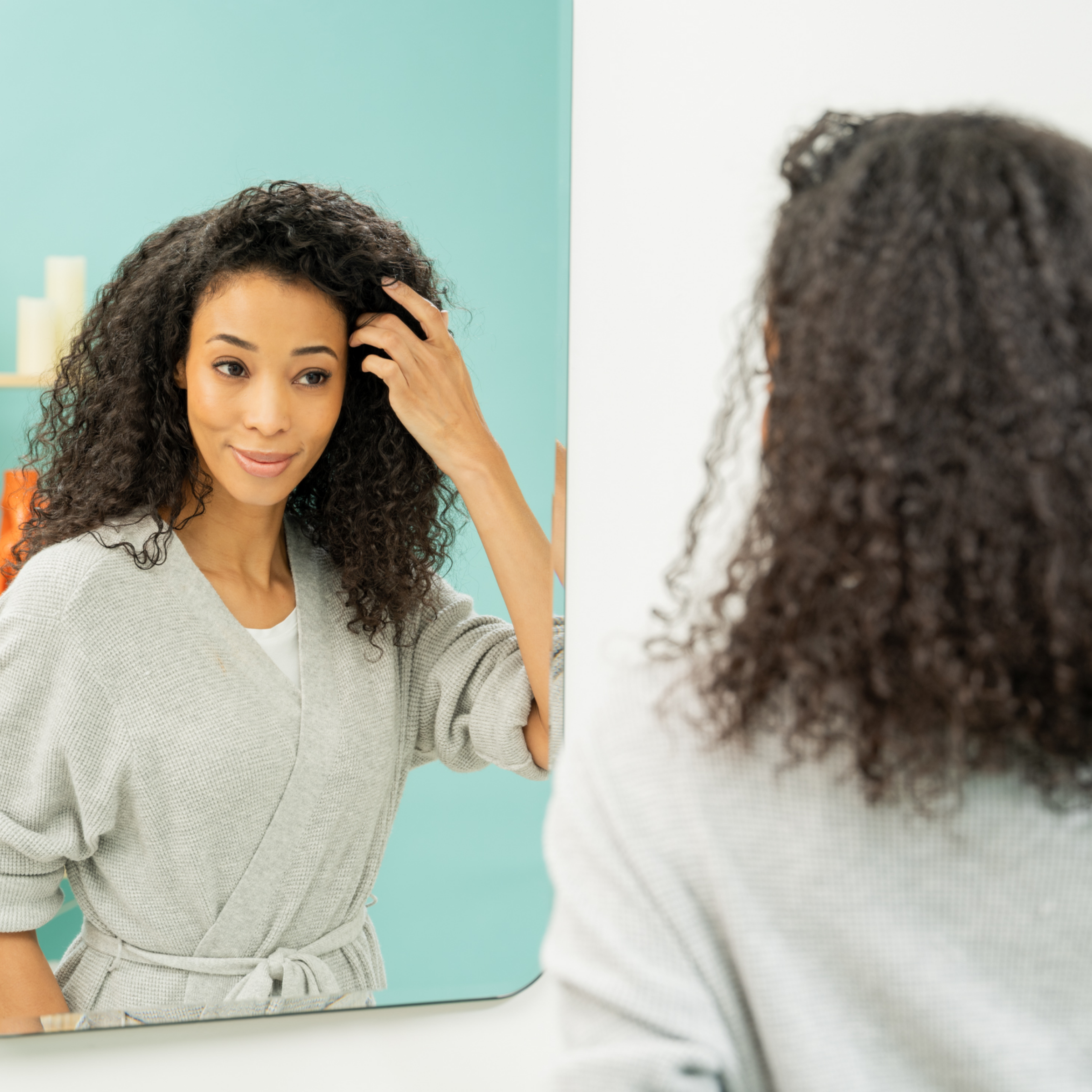 Woman in bathrobe looks in mirror while running her hand through her hair with tight curls