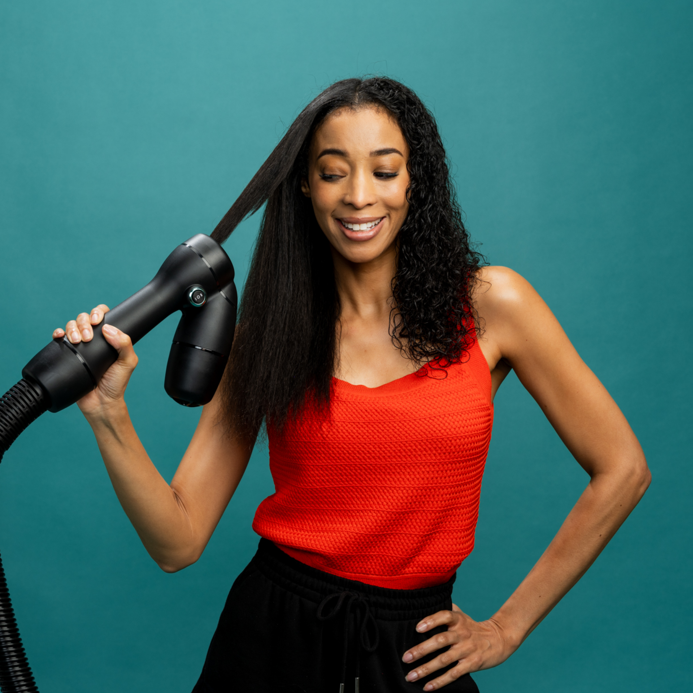 Woman in stylish summer outfit with one hand on hip uses the RevAir dryer to dry and stretch one side of her hair while the other remains wet and curly.