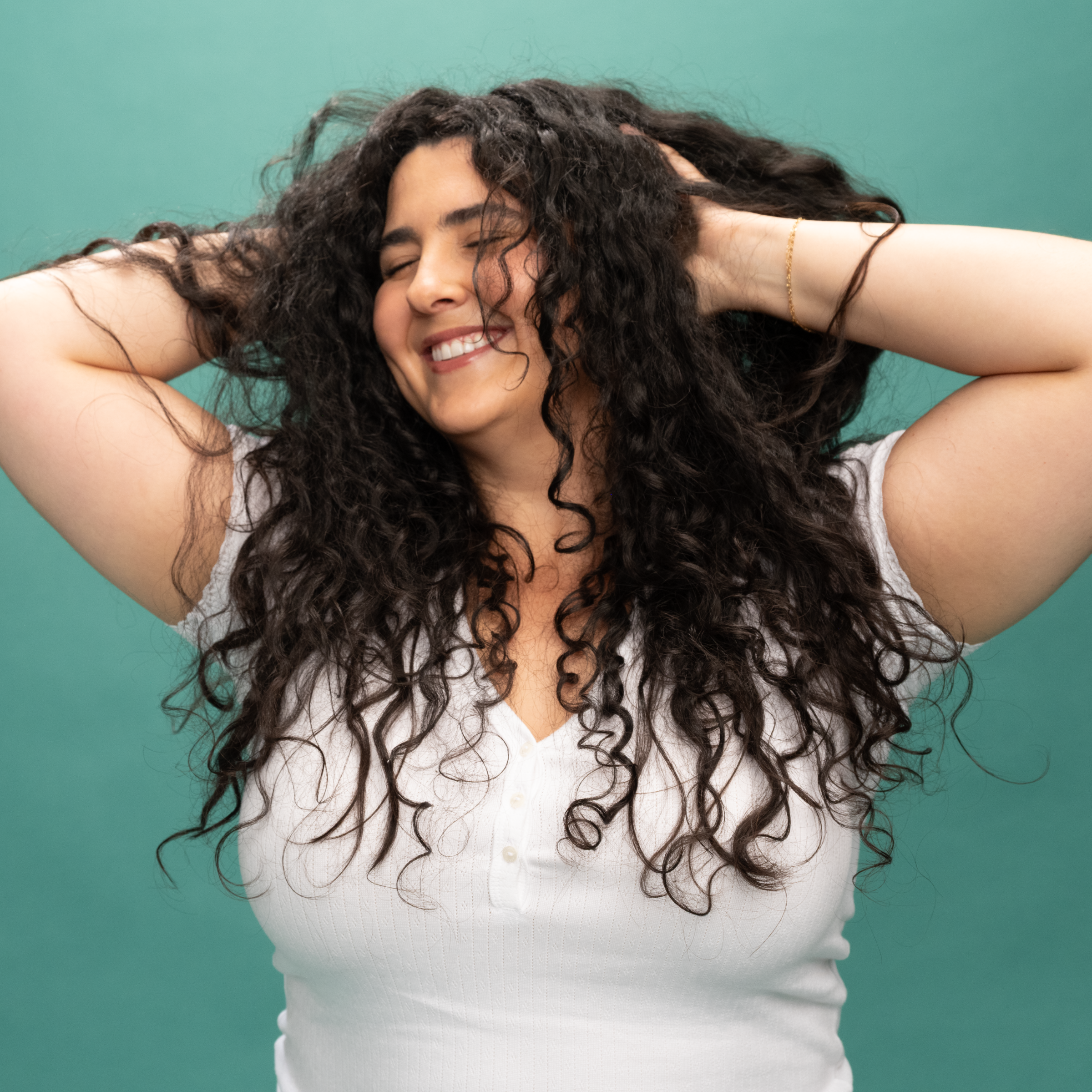 Smiling woman with eyes closed and long curly hair, her hands pushing her hair up into a fun, messy style