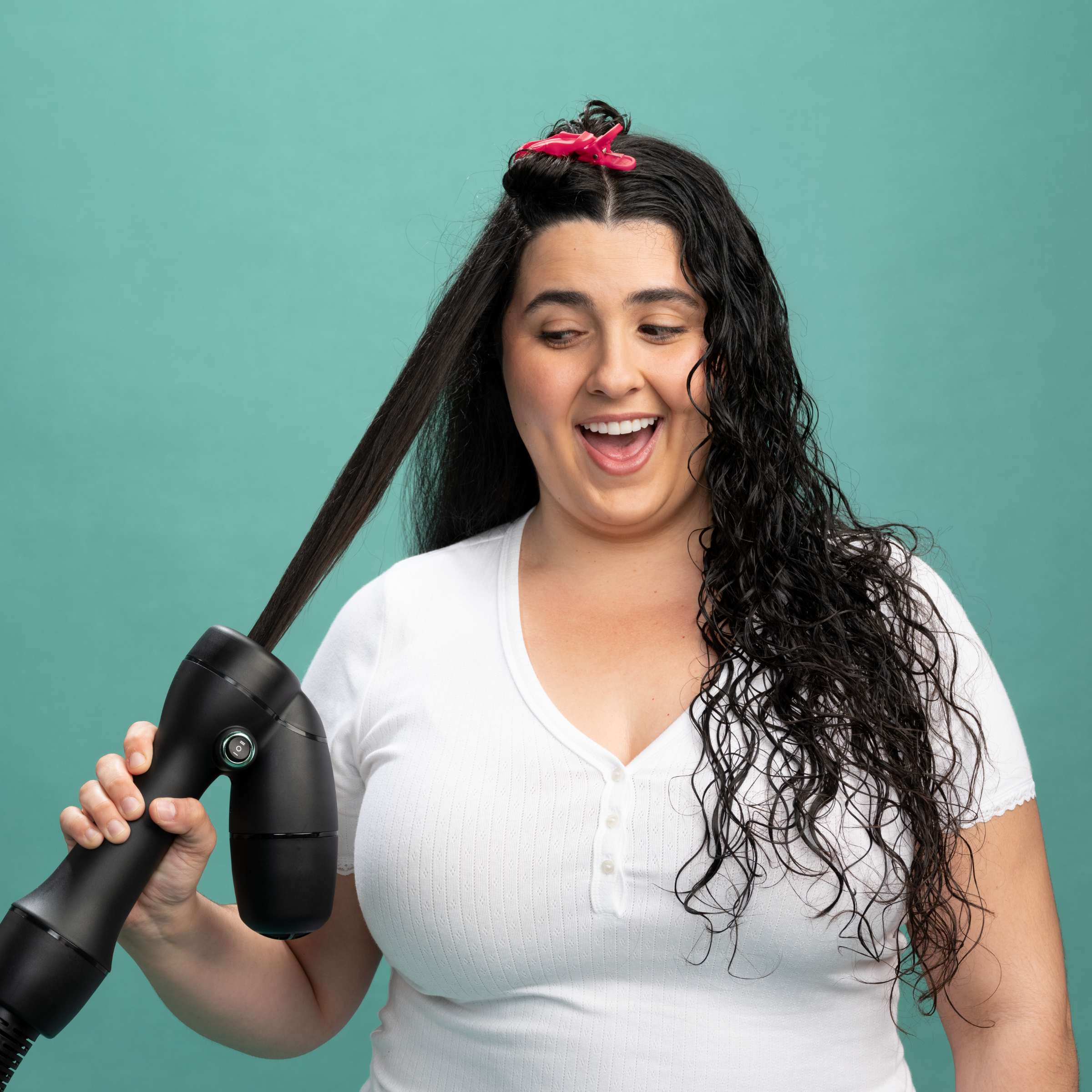 Woman using the RevAir dryer, with one side of her hair being dried and stretched by the wand, while the other side is still wet and curly