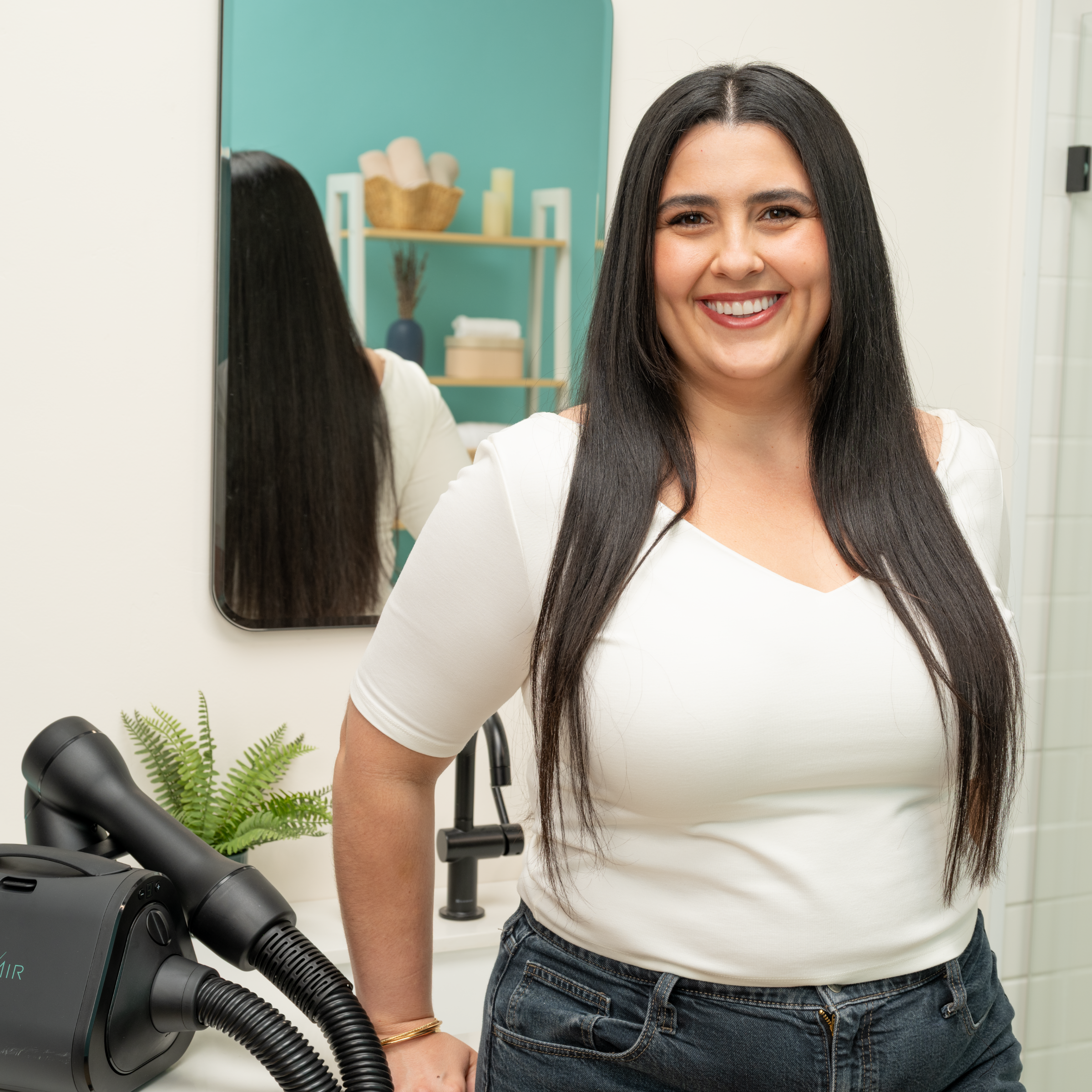 Smiling woman with long, stretched hair leaning back against bathroom with RevAir on counter.