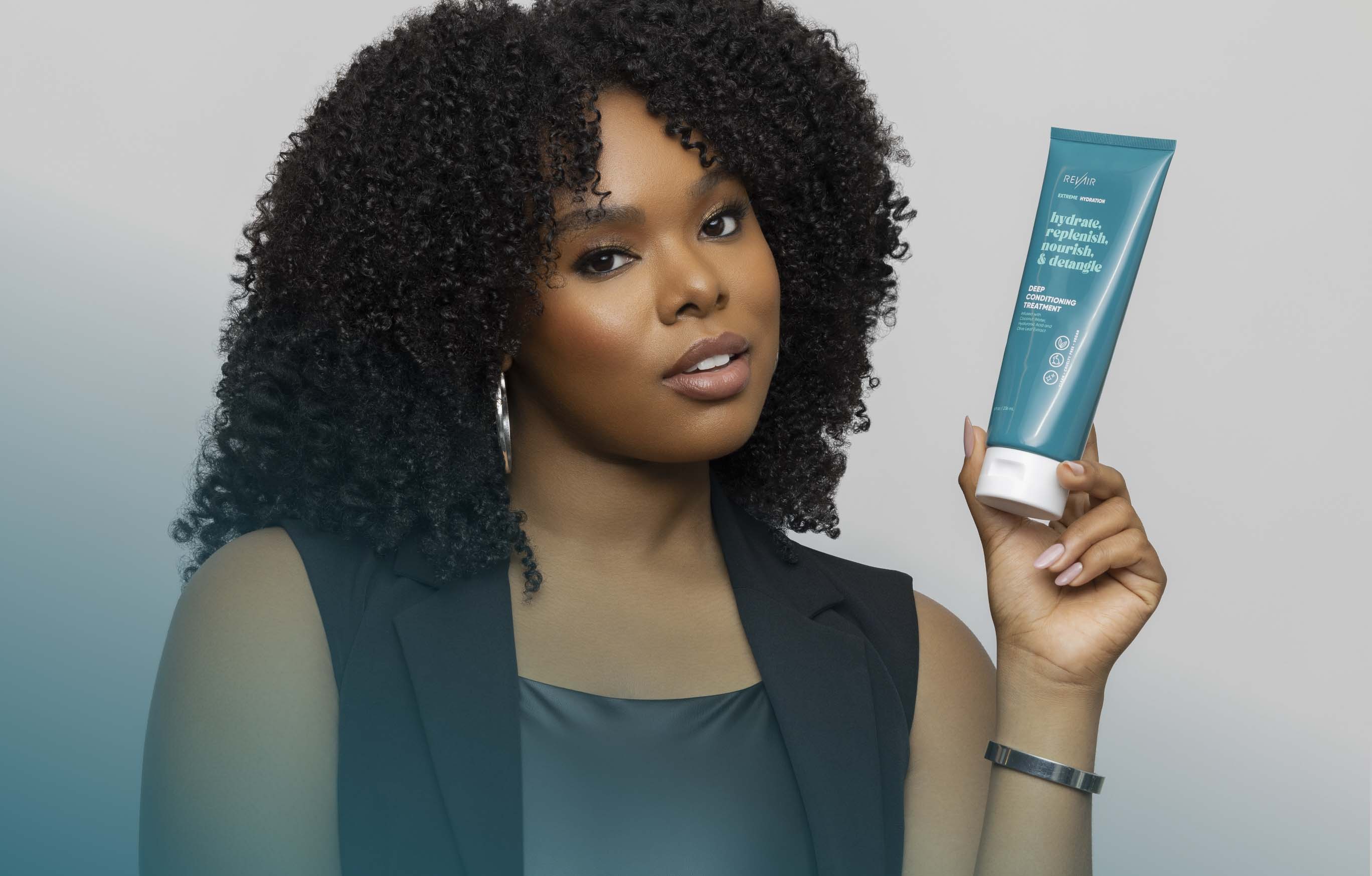 Woman with type 4 coily hair holding up bottle of deep conditioning treatment