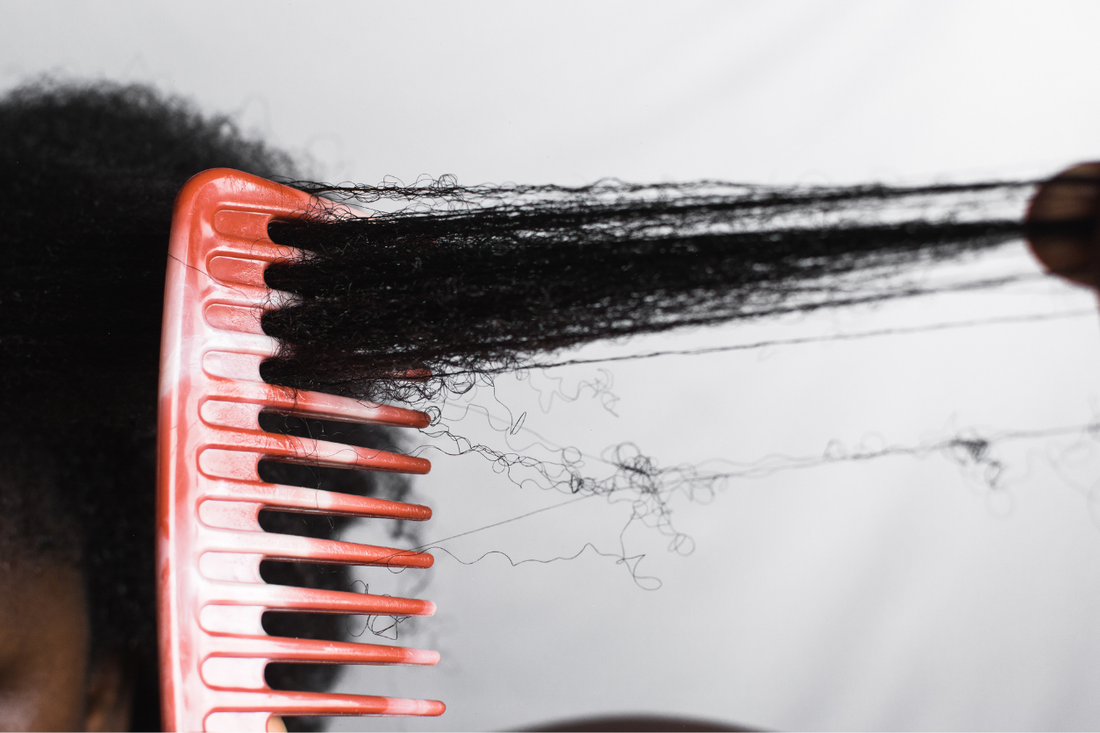 Close-up of a wide-tooth comb gently detangling a section of tightly coiled natural hair, showing strands stretched between the comb and hand.