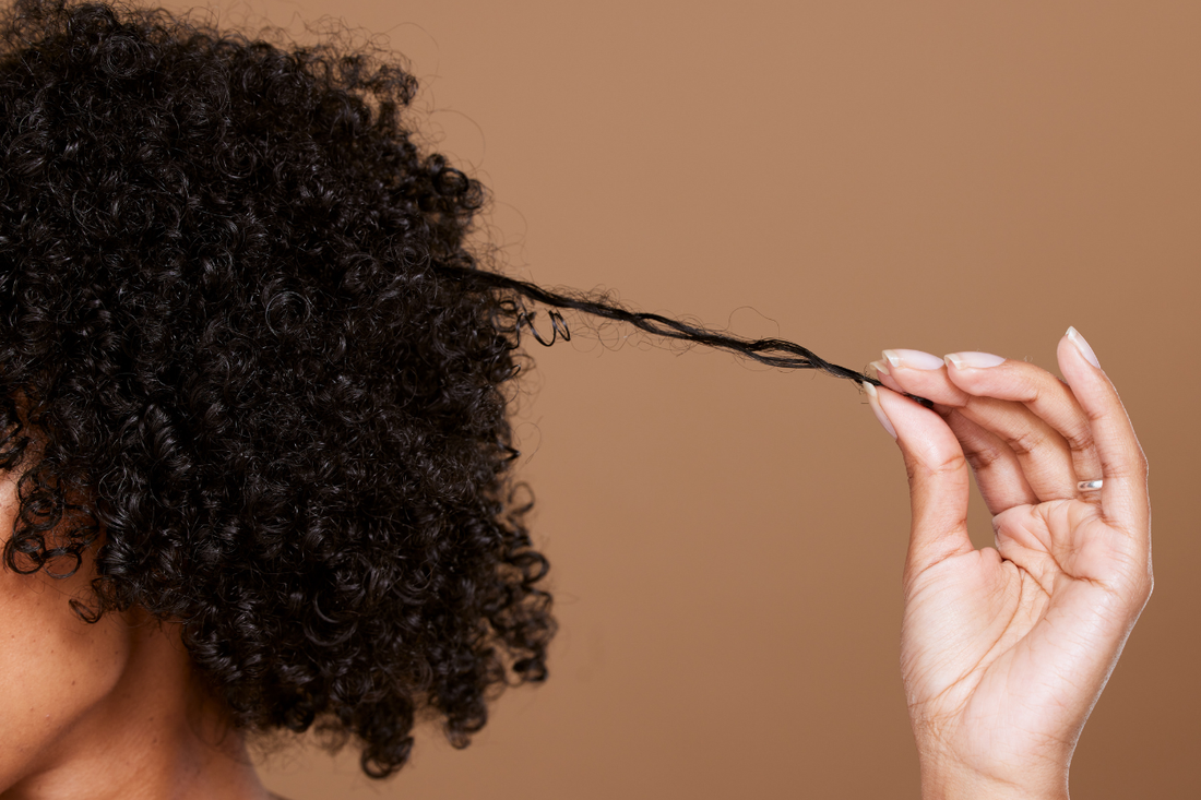 Woman stretching a single coil away from her dense natural hair to show strand thickness