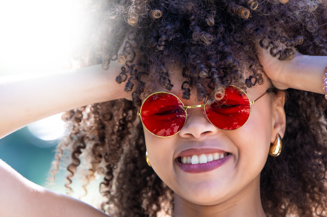 Smiling woman with defined afro puffs and flat twists, styled for summer humidity control, against a warm beige background.