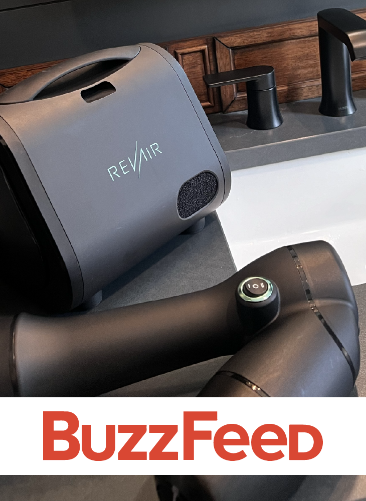 RevAir Reverse-Air Dryer unit and wand resting on a bathroom counter next to a black faucet, with the BuzzFeed logo displayed below