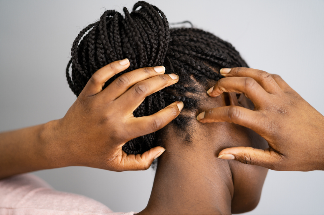 Hands parting braided hair at the nape of the neck to examine the scalp before installing a protective style.