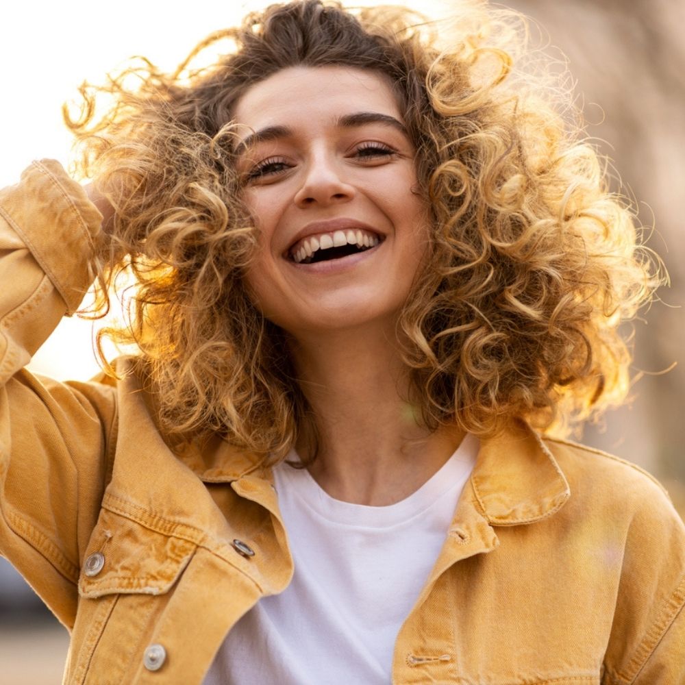 caucasian woman with light curly hair smiling at the camera