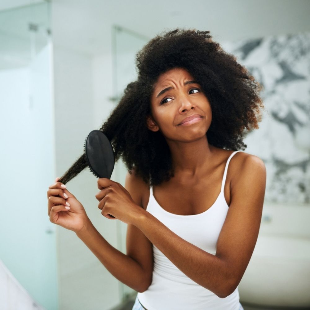 black woman with natural hair frowning while she brushes it out