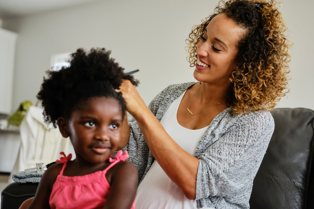 Mother gently detangling her daughter’s natural hair with a wide-tooth comb during wash day at home.