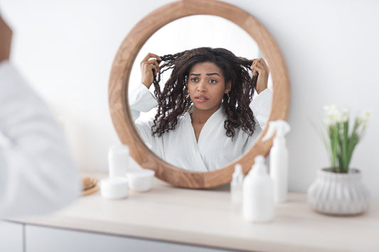 woman-in-white-holding-her-hair-while-looking-at-reflection-on-round-mirror-in-bedroom-hair-loss-concept