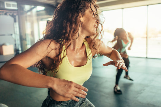 Woman with brown curly hair working out in the gym together with other women.