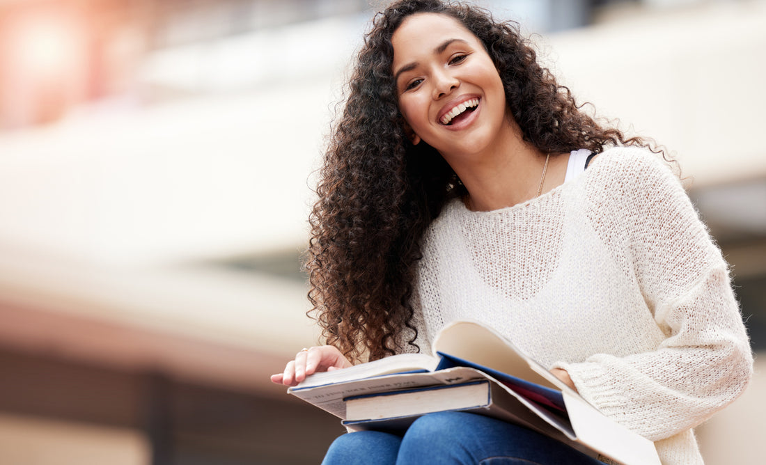 woman-holding-books-while-sitting-at-college-campus-back-to-school-hair-concept