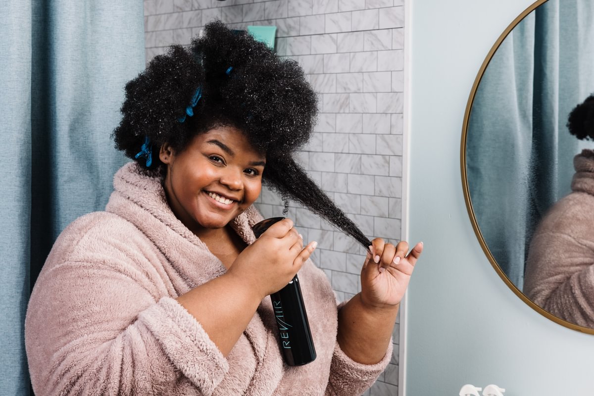 Woman in bathrobe smiling and spraying her hair with the Up and Atomizer Spray Bottle