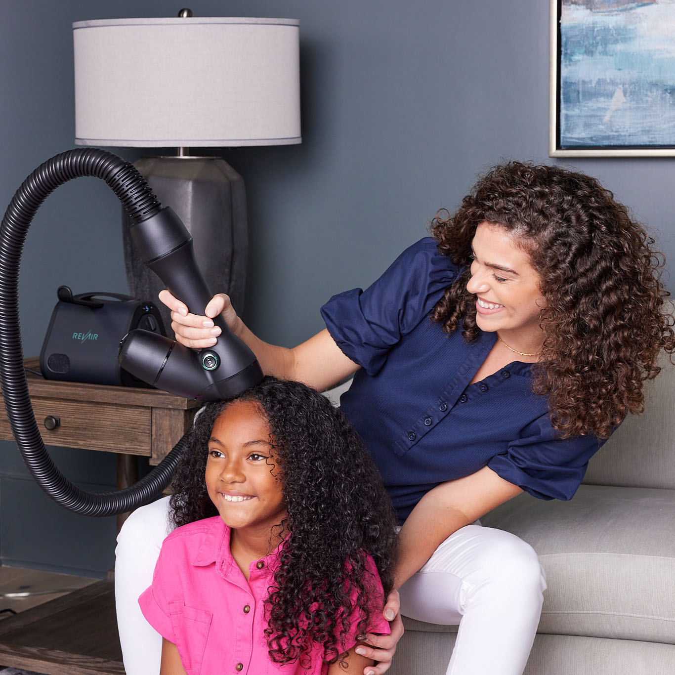 Mother and daughter sitting together and smiling while the mother dries her daughters hair with the RevAir dryer