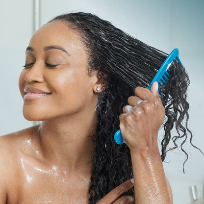 Woman in shower smiling and combing deep conditioning treatment product through her hair