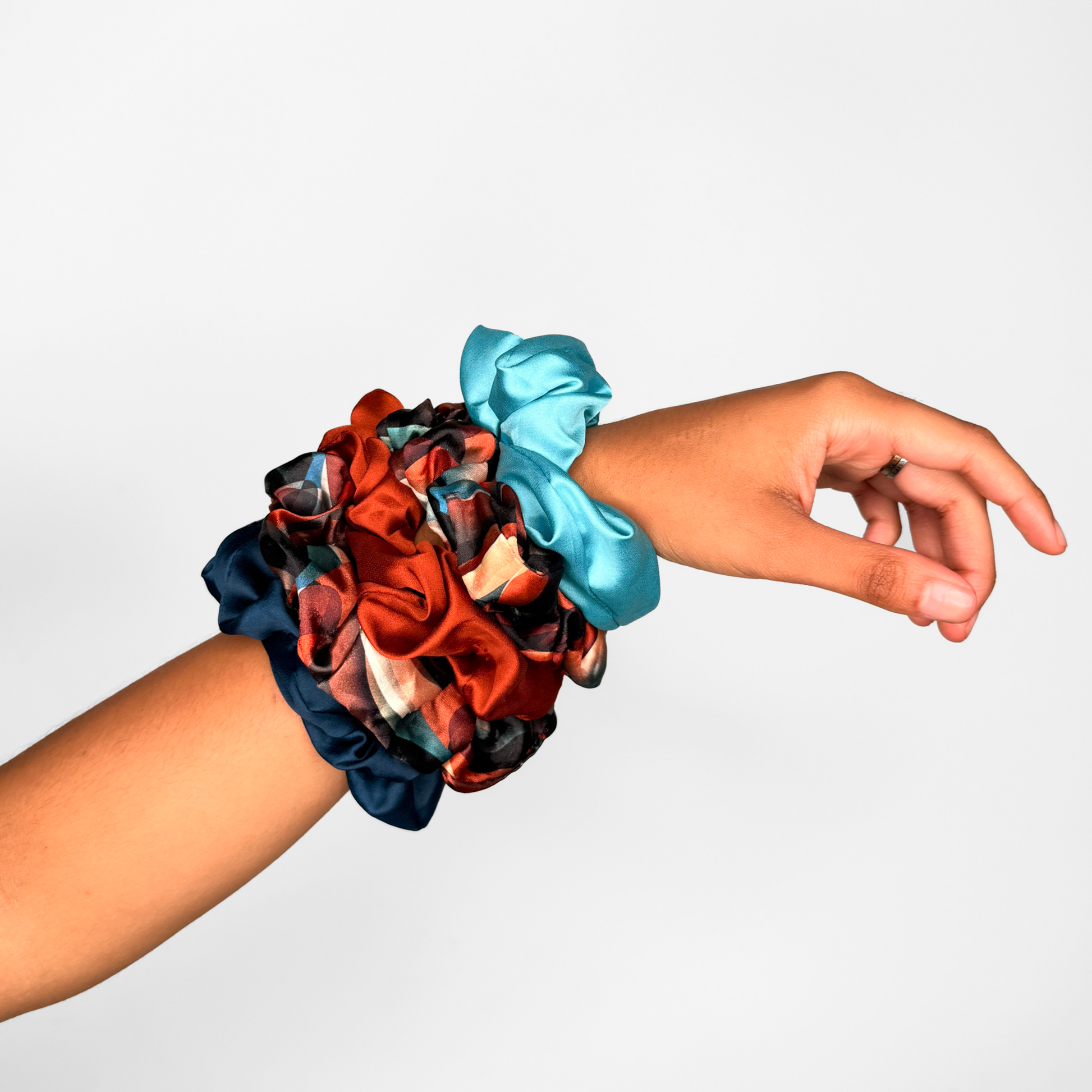 Hand wearing two scrunchies, one multicolored and one blue, on a light gray background