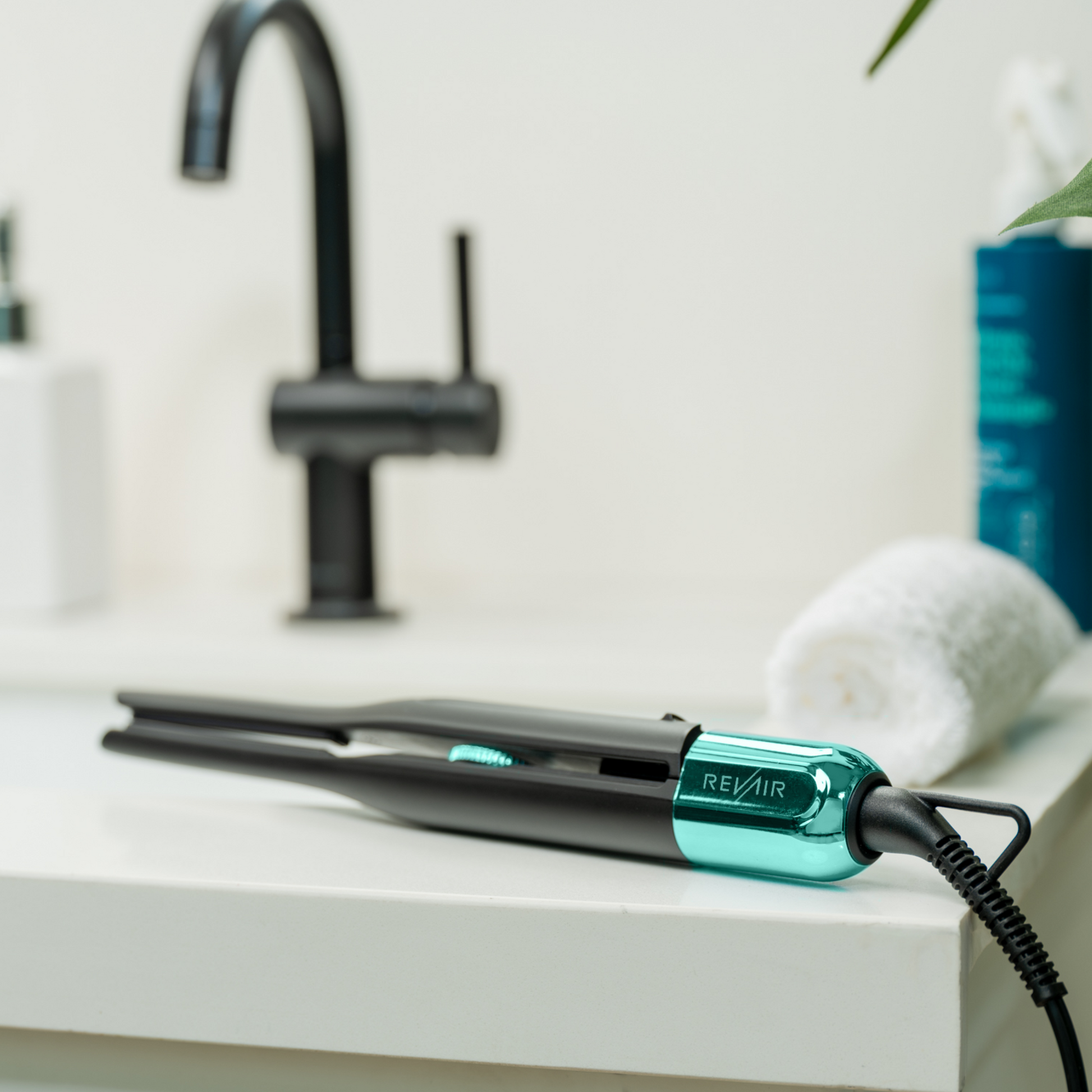 RevAir Micro Edge Styler pencil straightener on bathroom counter, sleek black and teal design with digital temperature control.