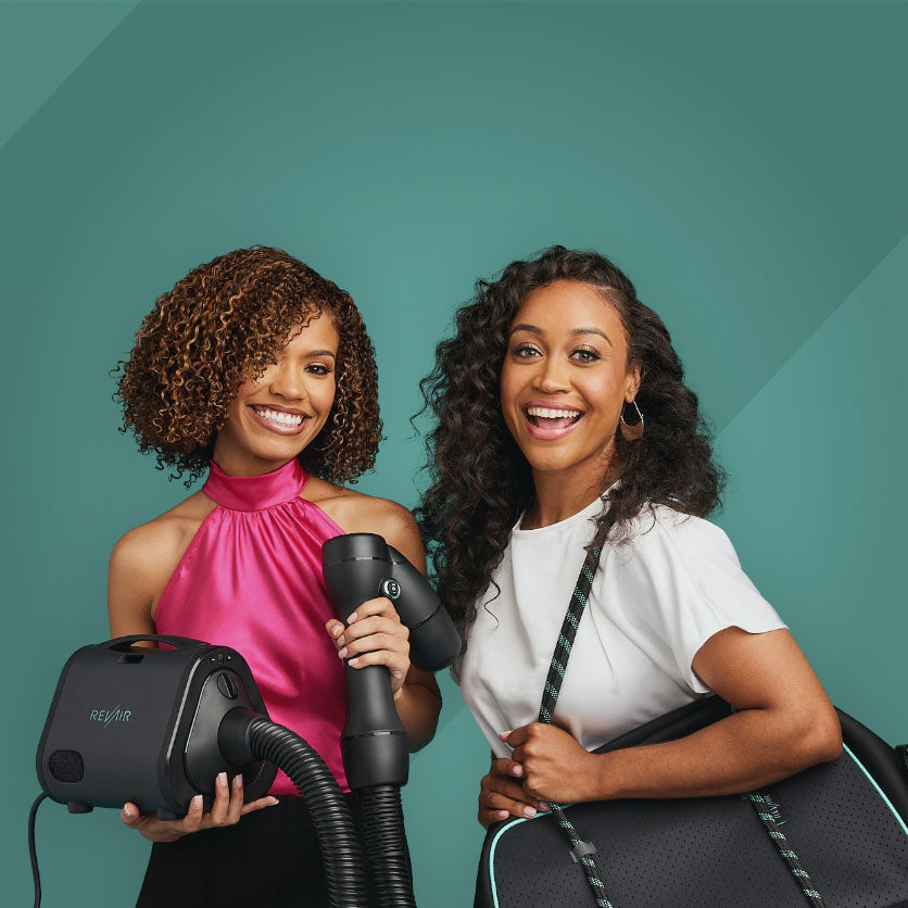 Two smiling women holding the RevAir reverse air hair dryer and weekender bag