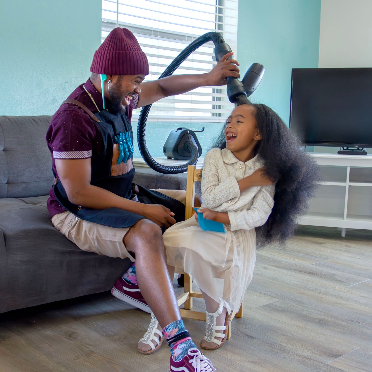 Father and daughter laughing and smiling as he uses RevAir on her hair in their living room.